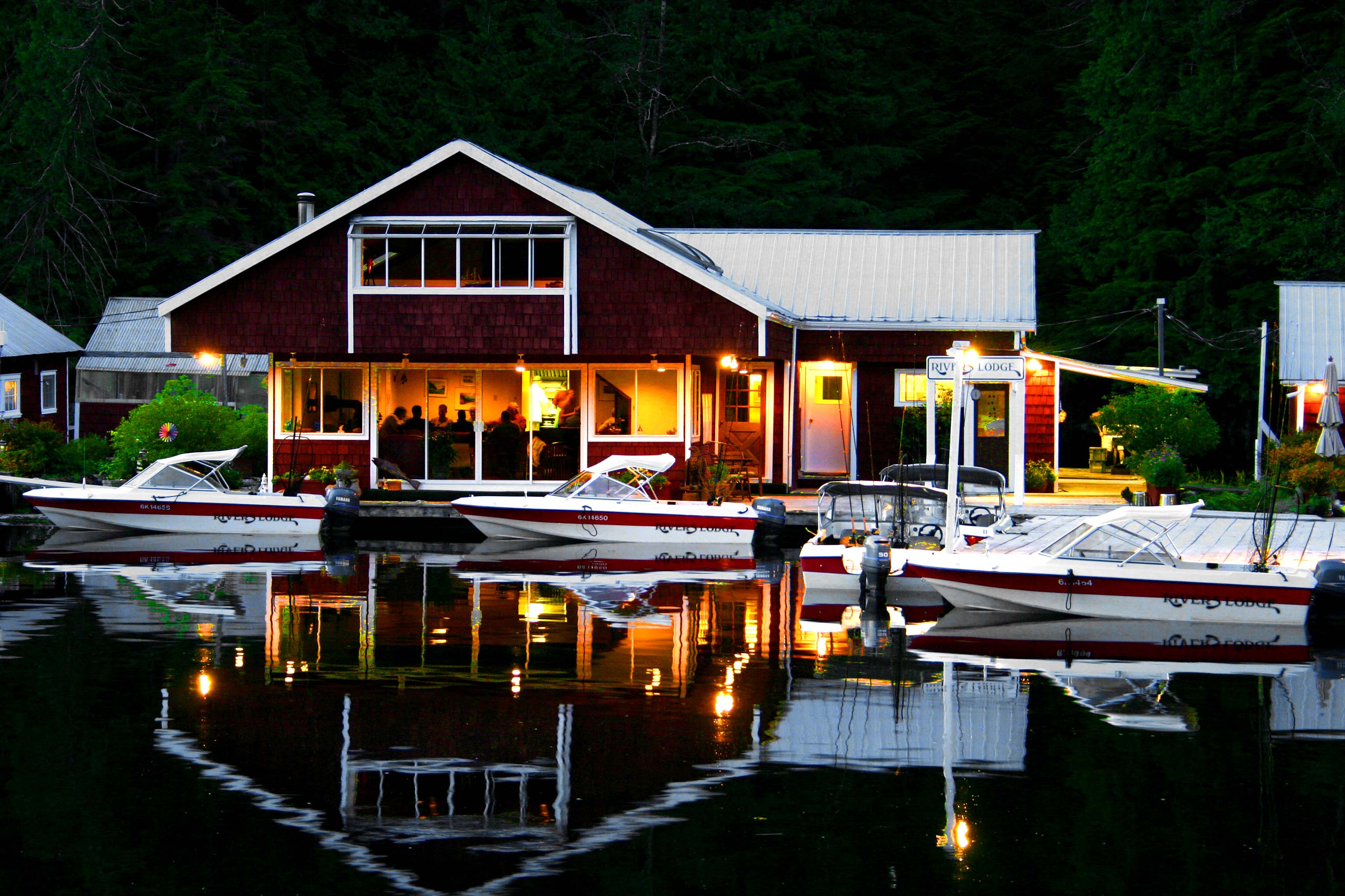 Lodge buildings glowing with warm lights at dusk, boats moored peacefully