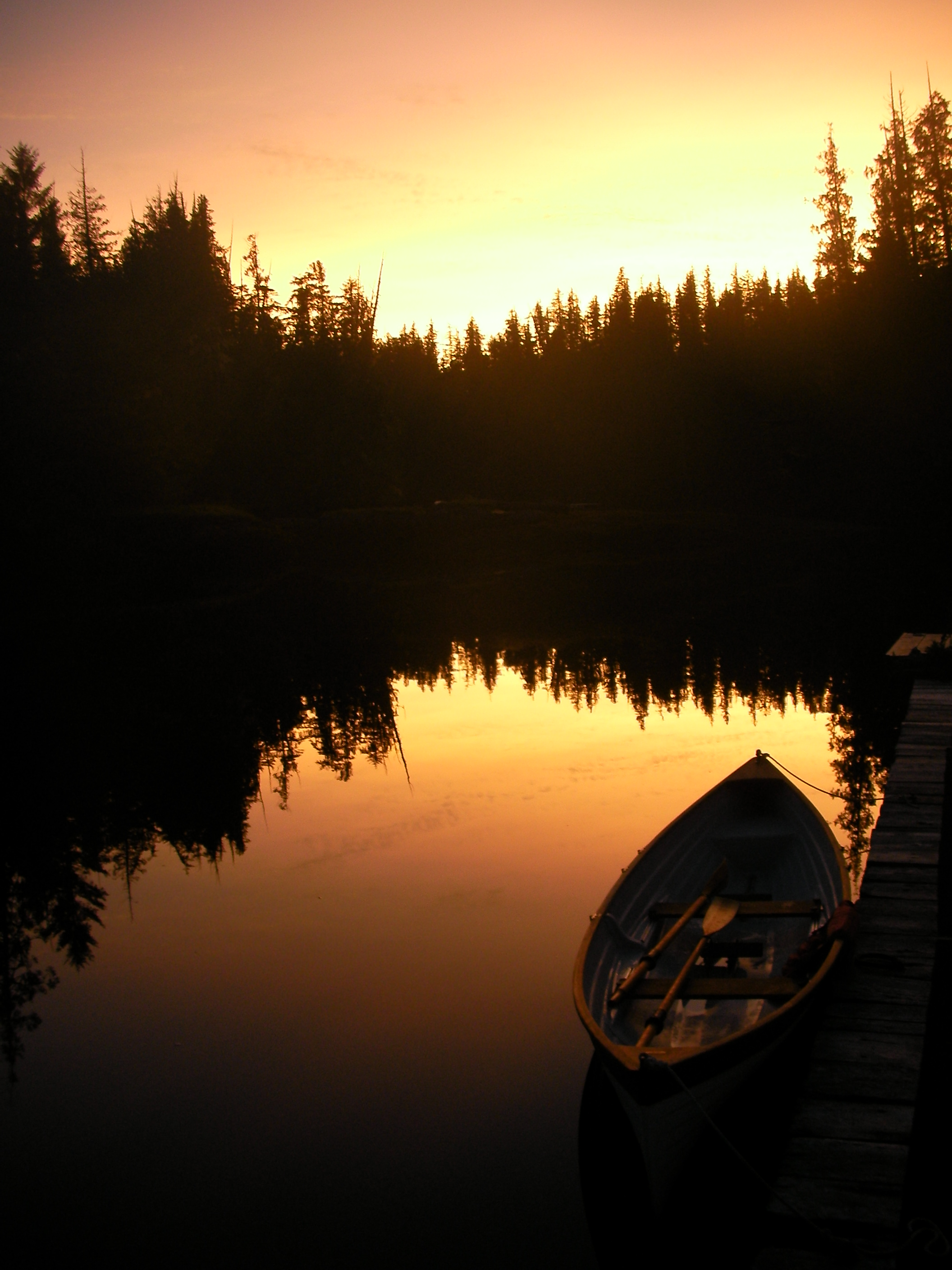 Small boat on calm water at sunset with forest silhouette